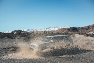 A vibrant action shot of a lifted side-by-side tearing through a muddy rock trail under bright sunlight.