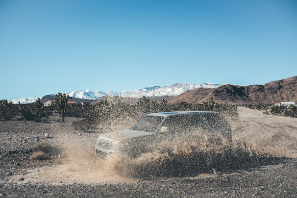 A vibrant action shot of a lifted side-by-side tearing through a muddy rock trail under bright sunlight.