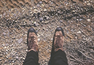 person wearing brown shoes standing on dirt and stone ground