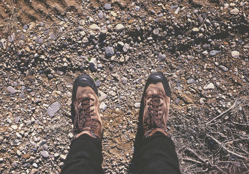 person wearing brown shoes standing on dirt and stone ground