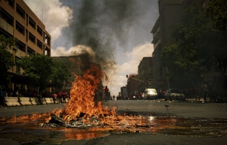 fire burning on the road with high rise buildings during daytime photography