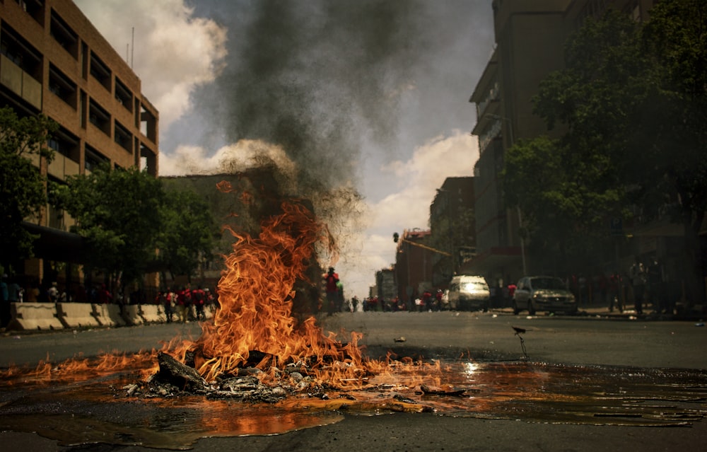 fire burning on the road with high rise buildings during daytime photography