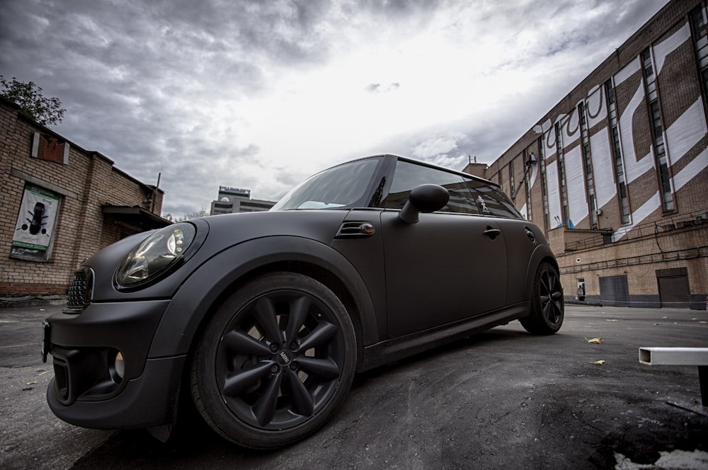 matte-black Mini Cooper near brown commercial buildings