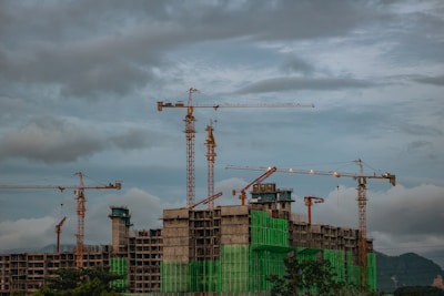 A skilled contractor measuring and planning a modern building site under a moody sky.