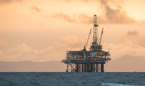 A sturdy offshore oil rig silhouetted against a deep blue sky at dusk.
