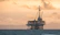 A confident offshore worker in safety gear standing on a drilling platform at sunset.