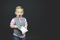 boy wearing gray vest and pink dress shirt holding book