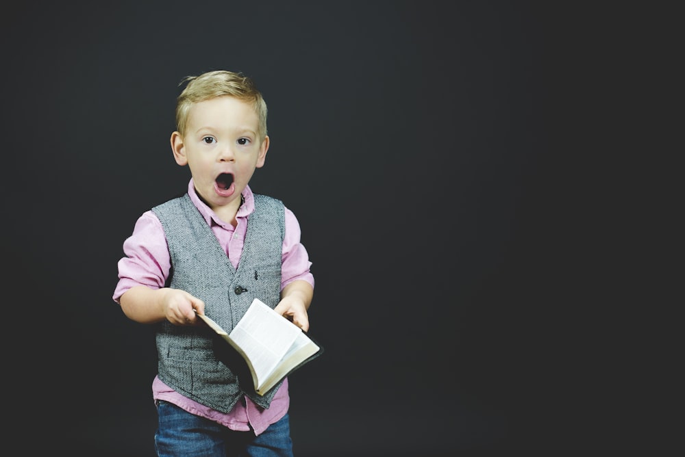 boy wearing gray vest and pink dress shirt holding book