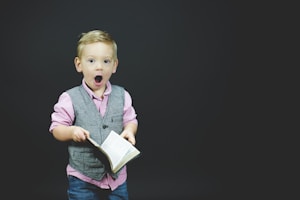 boy wearing gray vest and pink dress shirt holding book