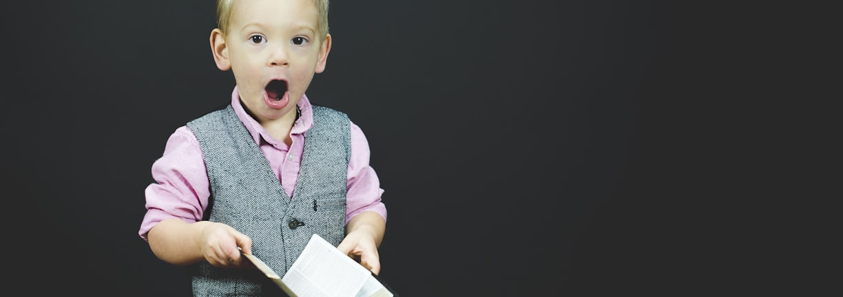 boy wearing gray vest and pink dress shirt holding book