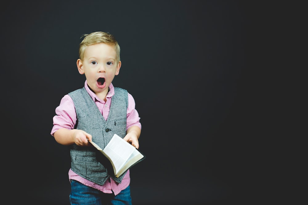 A little boy holding a book with a surprised expression on his face