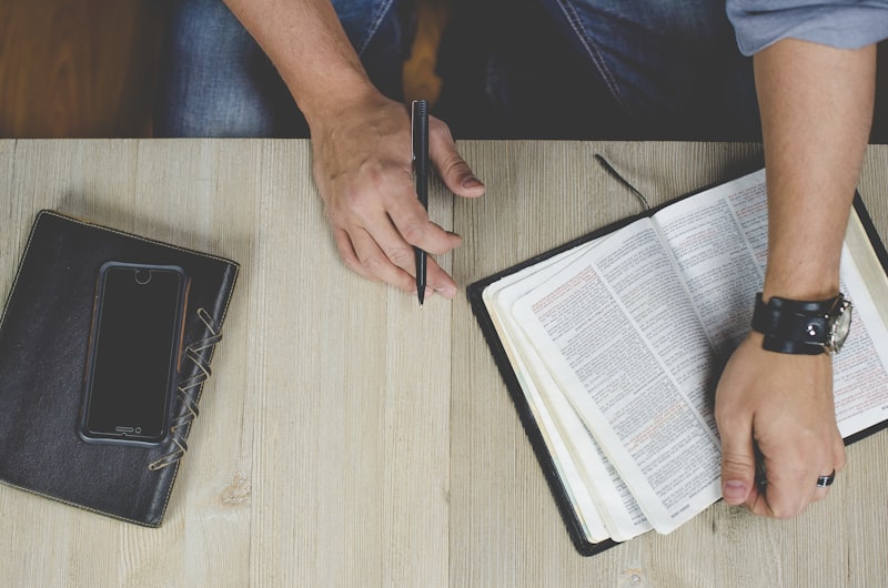 Person reading a Bible and holding a pen.