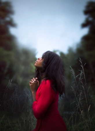 woman wearing red sweatshirt looking at top between trees near grass during daytime