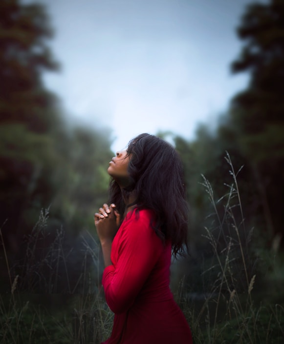 woman wearing red sweatshirt looking at top between trees near grass during daytime