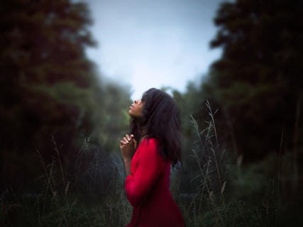 woman wearing red sweatshirt looking at top between trees near grass during daytime