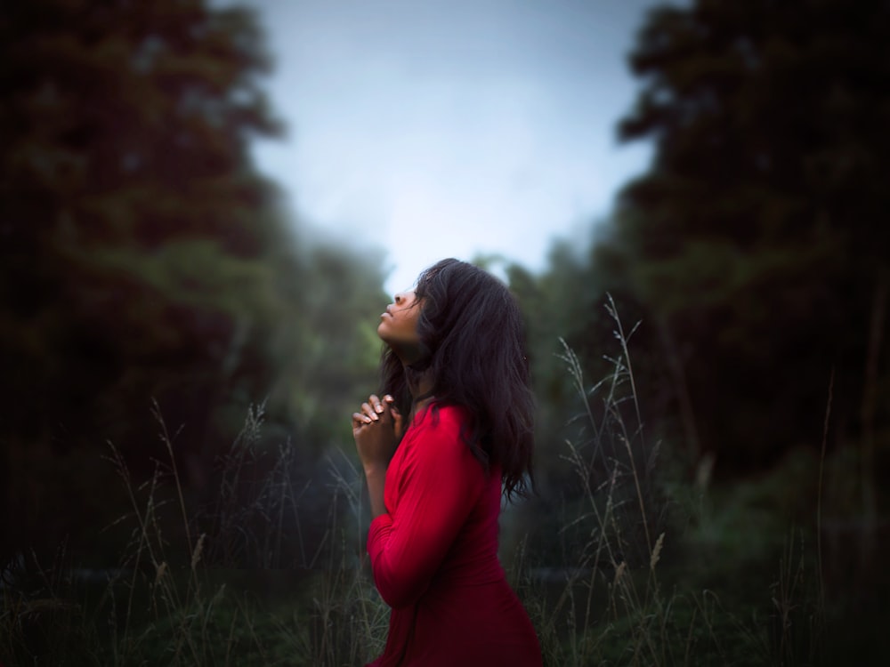 woman wearing red sweatshirt looking at top between trees near grass during daytime