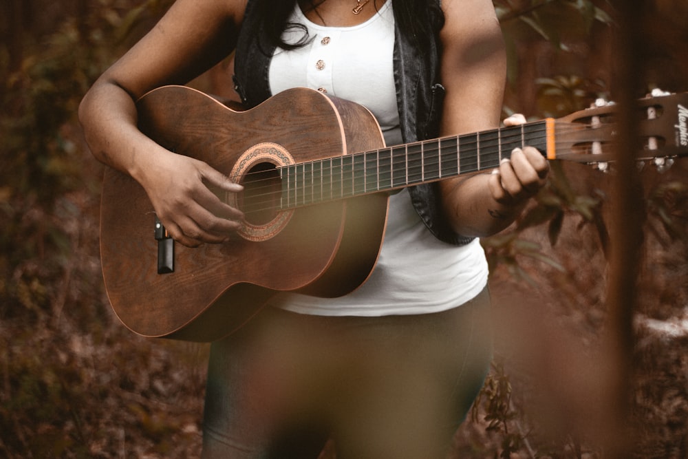A woman playing acoustic guitar with leaf-covered ground in the background