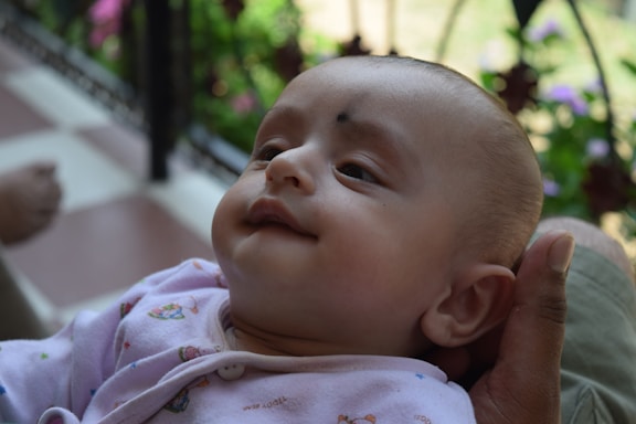 A soft pastel illustration of a baby holding a phone with a gentle smile.