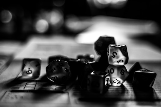 A collection of polyhedral dice scattered across a table with a blurred background, capturing a sense of mystery and focus on tabletop gaming.
