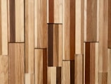 A collection of wooden planks arranged vertically with a variety of natural wood tones. The planks are of different widths and the texture of the wood grain is visible.