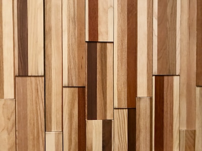 A collection of wooden planks arranged vertically with a variety of natural wood tones. The planks are of different widths and the texture of the wood grain is visible.
