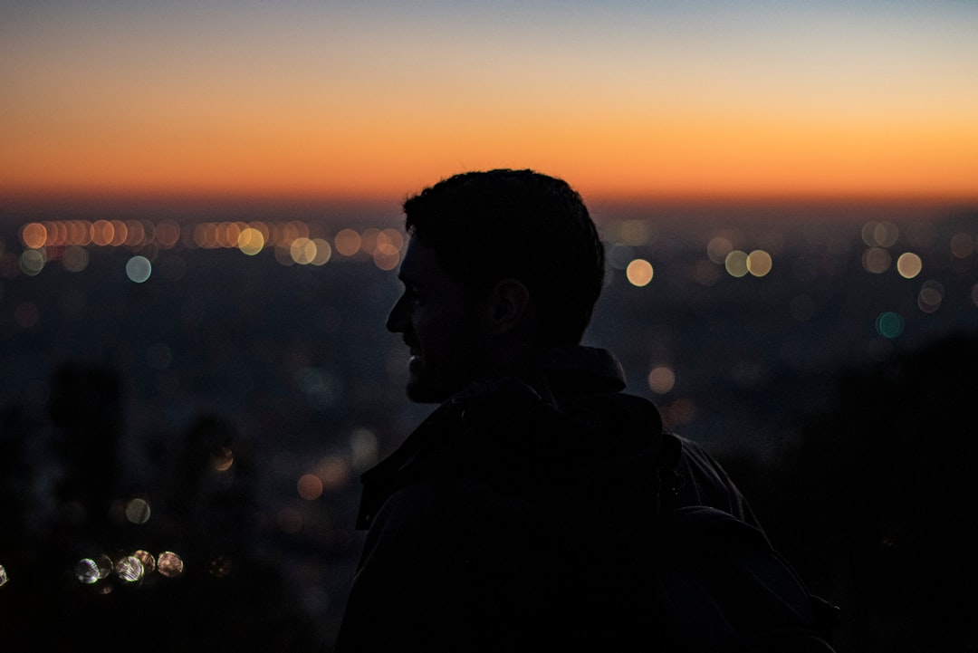 man on high ground facing right looking at city during nighttime