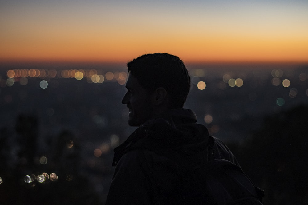 man on high ground facing right looking at city during nighttime