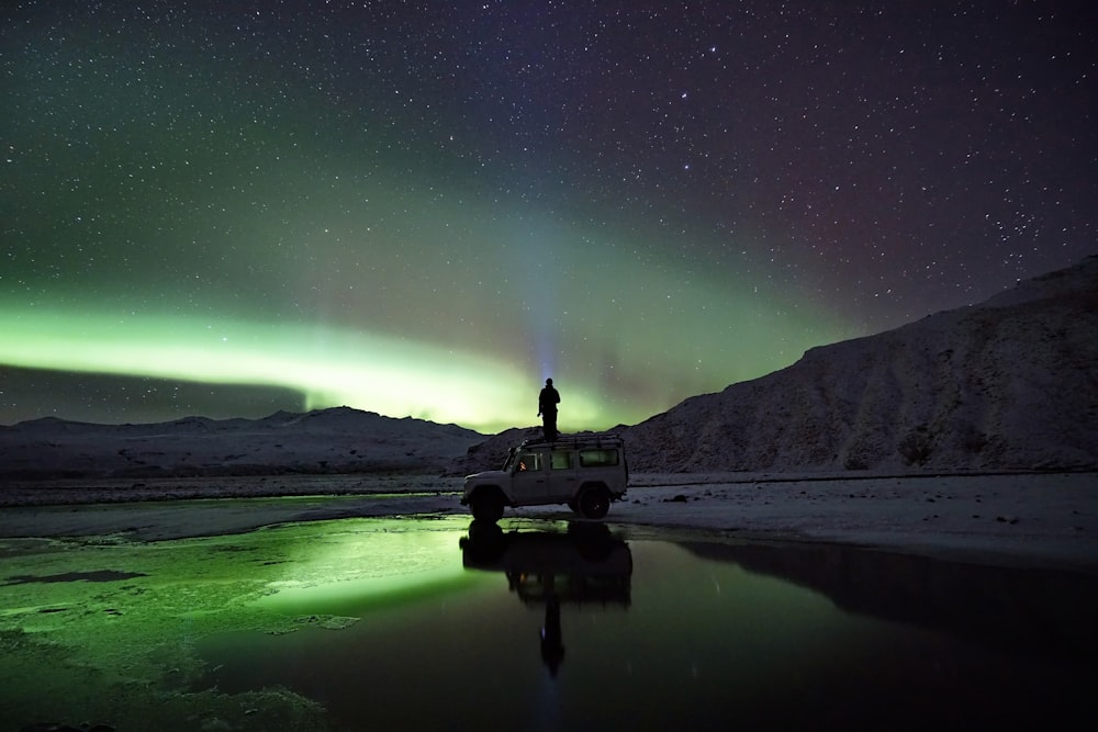 man standing on SUV watching northern lights