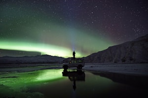 man standing on SUV watching northern lights