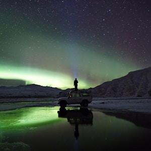 man standing on SUV watching northern lights