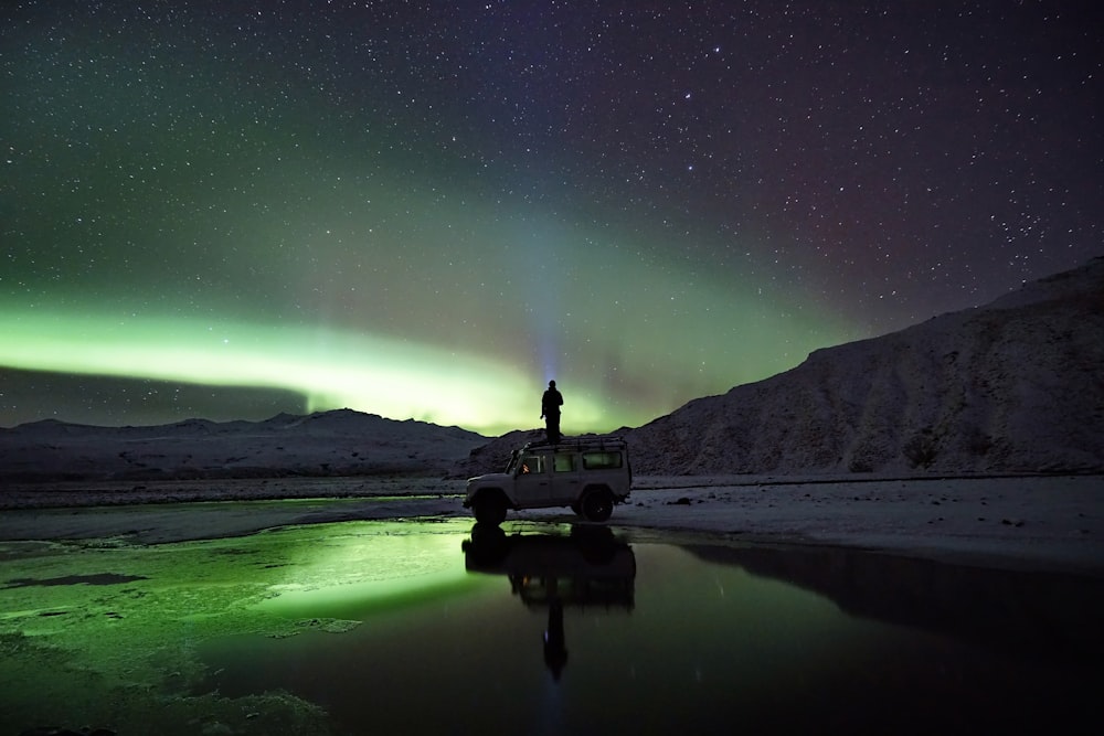 homem em pé no SUV observando aurora boreal