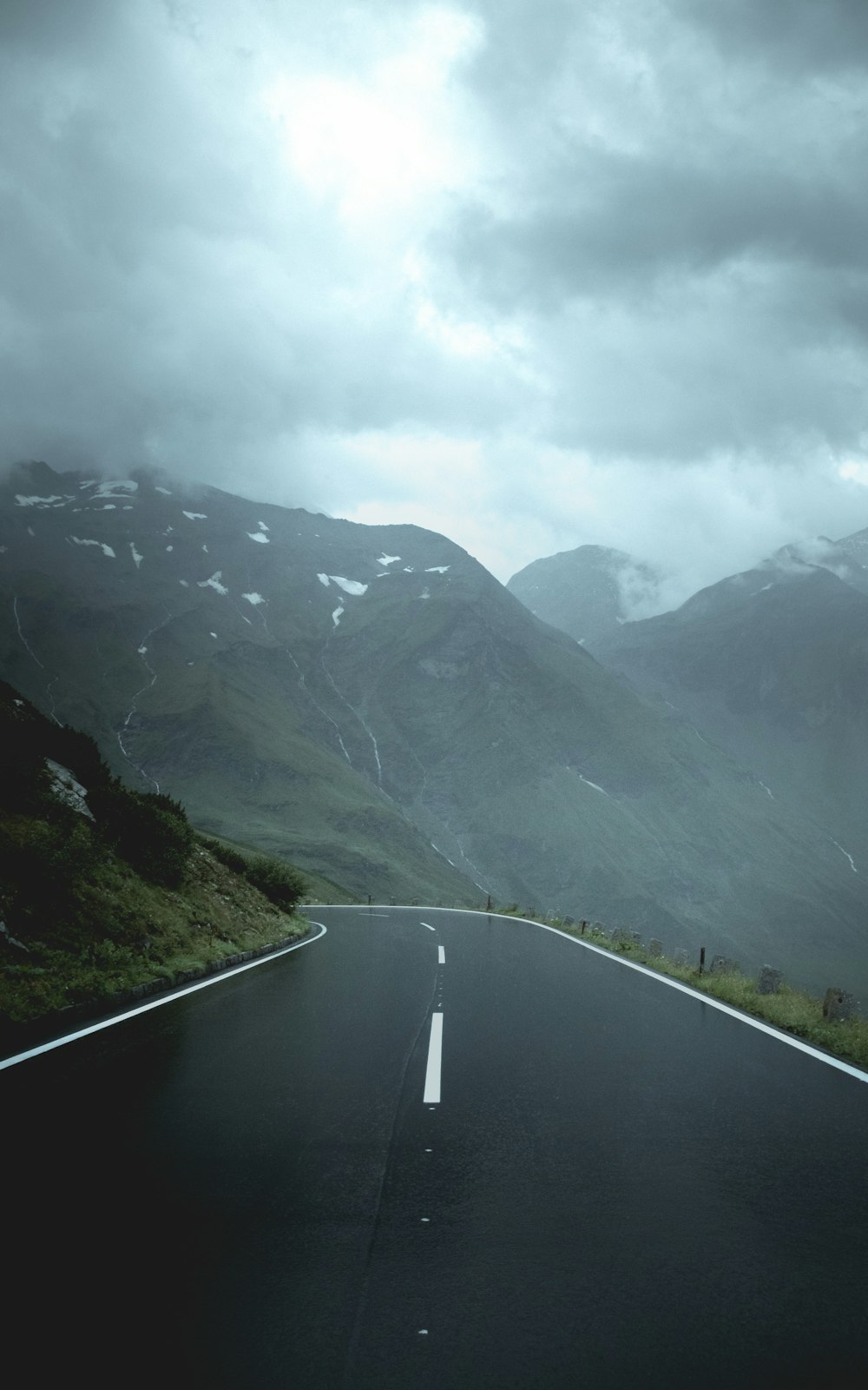 gray concrete road between green mountains under white clouds during daytime