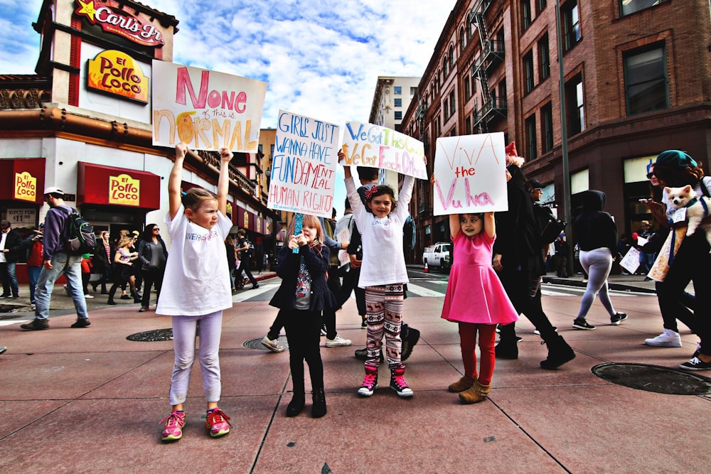 four children raising up a banner at the middle of a busy street during day time