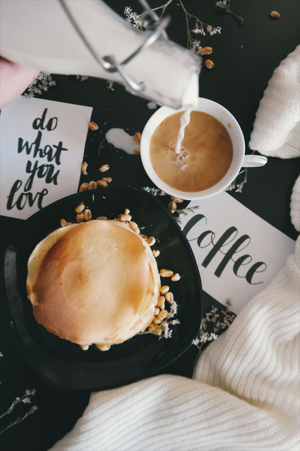 A plate of food with a cup of coffee, taken while someone pours sugar into the drink.