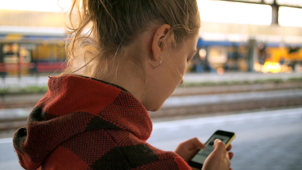 Eine Person steht an einem Bahnsteig und schaut auf ihr Smartphone.