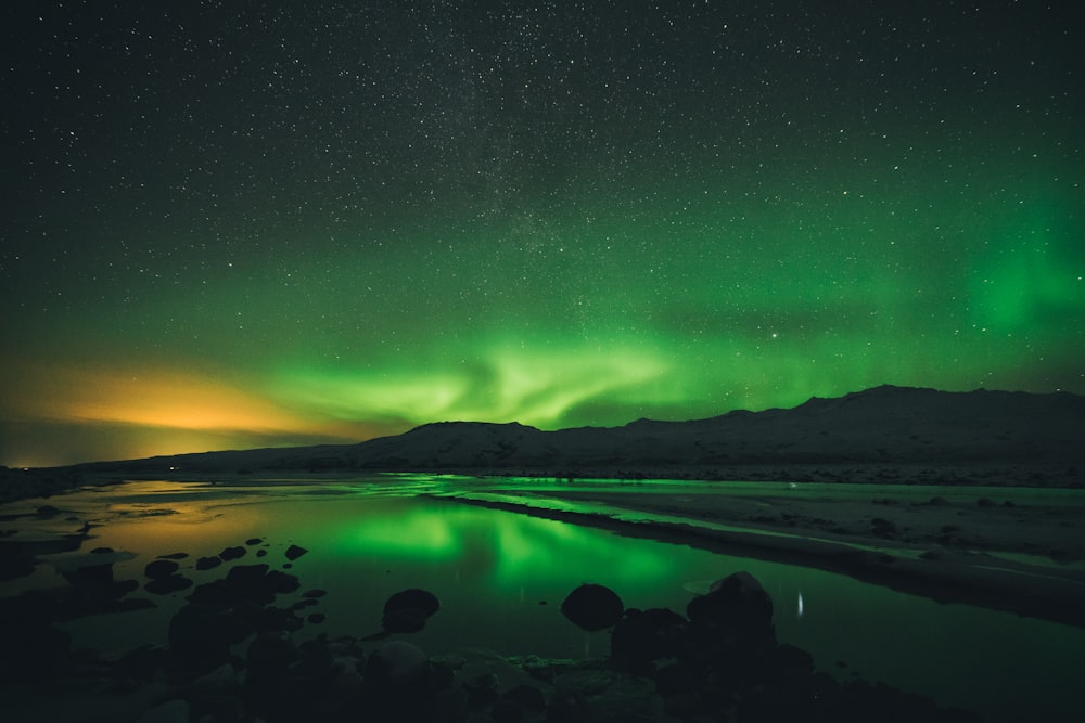 calma de água perto da montanha sob aurora boreal à noite