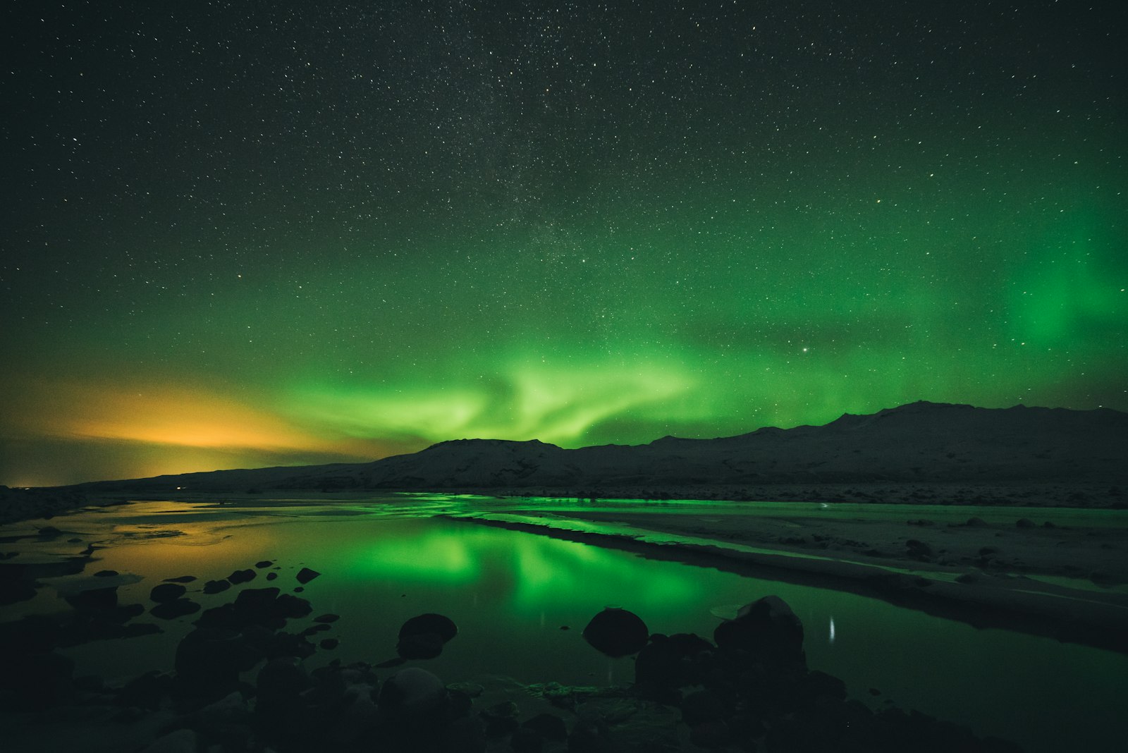 Aurora borealis reflected in calm Icelandic water with a mountain in the background