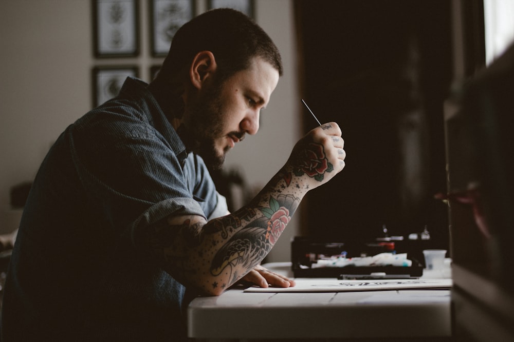 An artist with a tattoo on his arm working at a desk