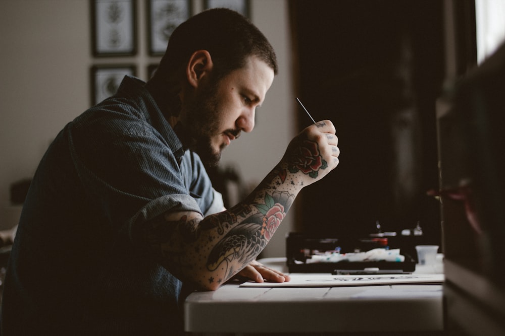 man holding pen and paper sitting near table facing outside in a dim-lit room during daytime