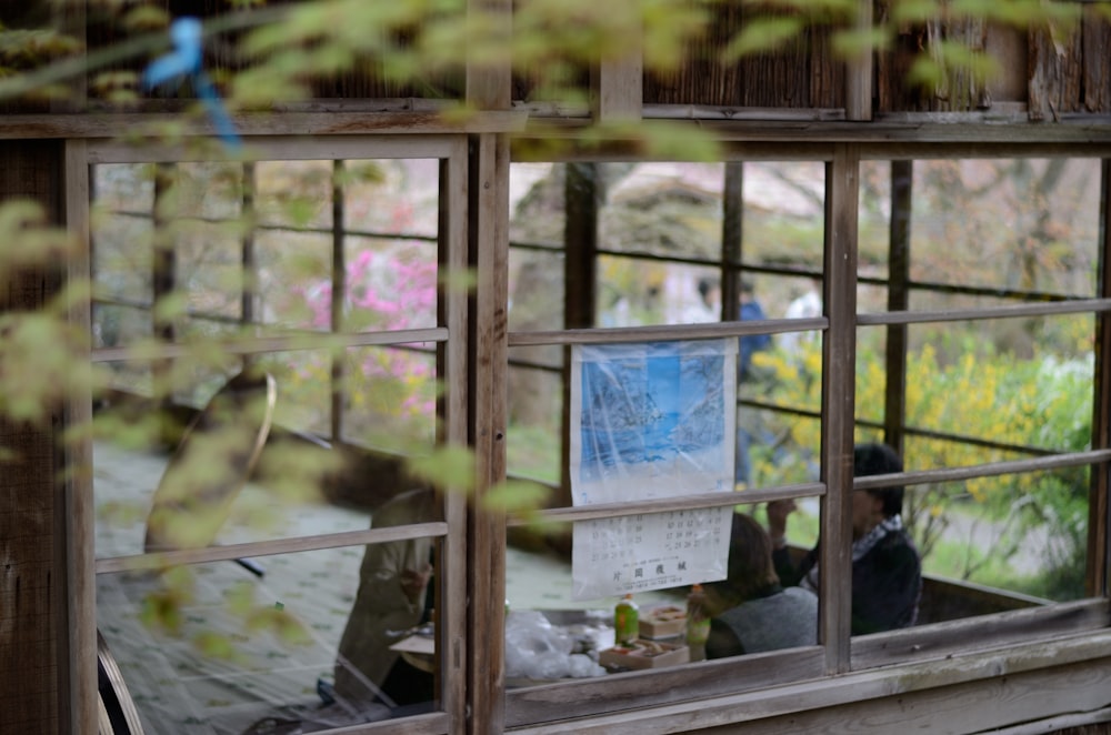 man and woman sitting down inside brown wooden room surrounded green plants during daytime