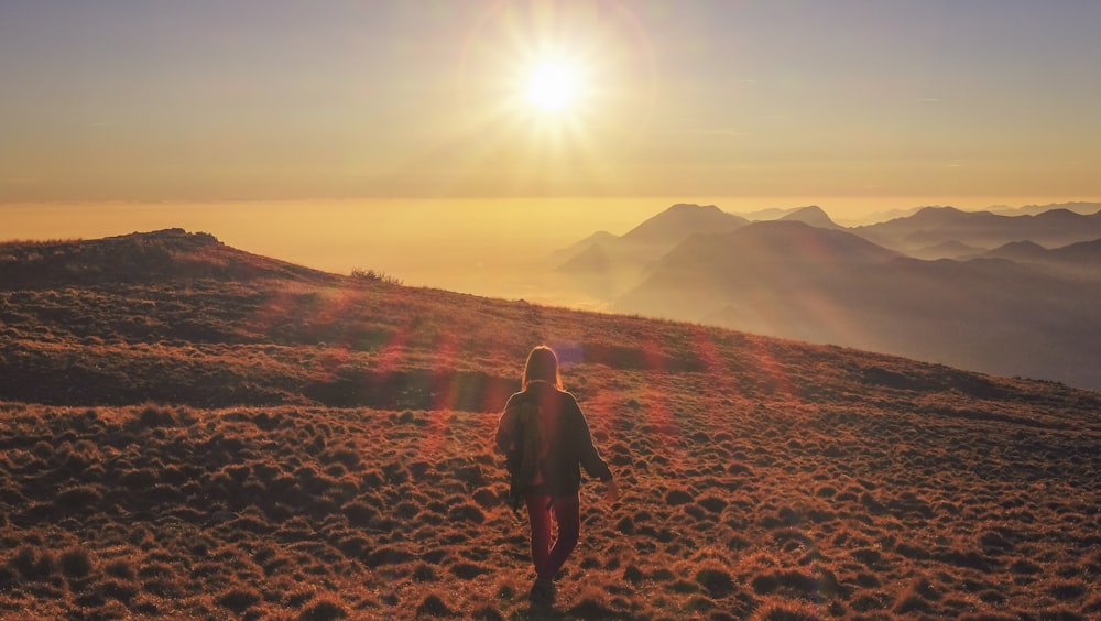 woman in blue jacket walking on desert during sunset