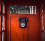black rotary telephone mounted on red wooden wall