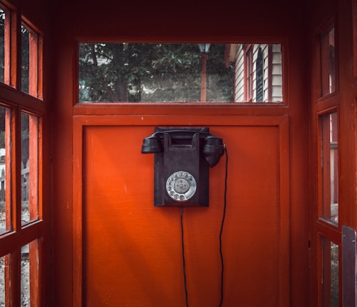 black rotary telephone mounted on red wooden wall