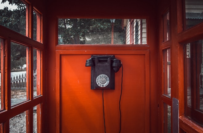 black rotary telephone mounted on red wooden wall