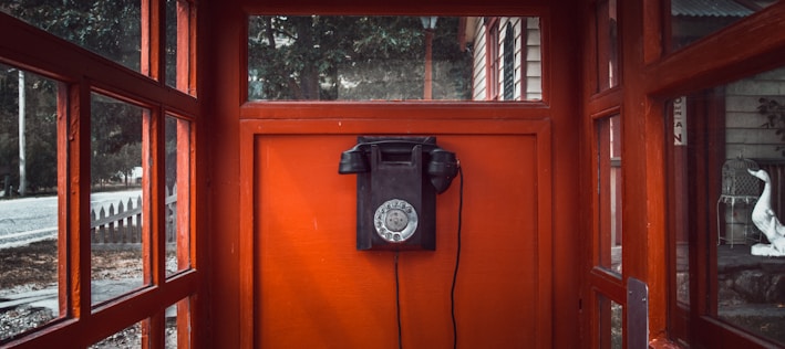 black rotary telephone mounted on red wooden wall