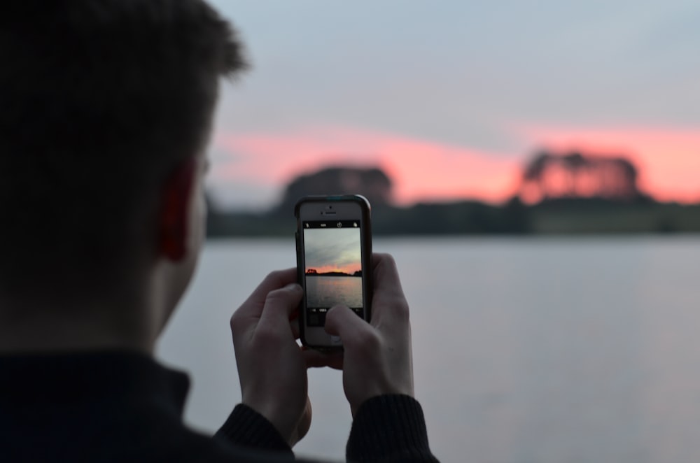 Fotografia a fuoco selettiva di una persona che utilizza la fotocamera dello smartphone che scatta foto dello specchio d'acqua blu