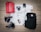 A selection of outdoor and travel items neatly arranged on a wooden surface, including a red jacket, two pairs of black hiking boots, a black backpack, a map, three cameras, a metal water bottle, a compass, a wristwatch, and a folding knife.