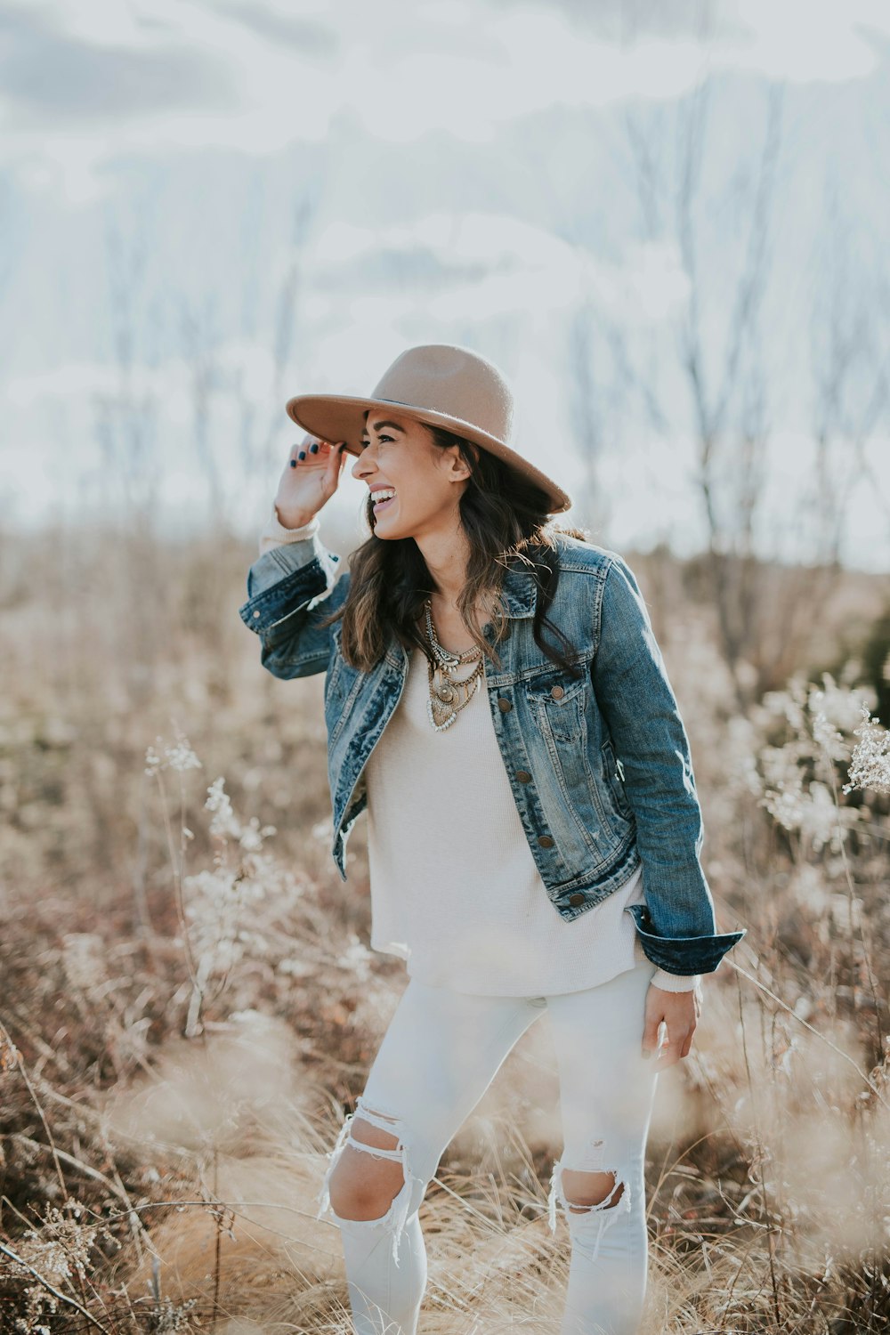 woman standing on dried grass facing right while holding her brown sun hat during daytime