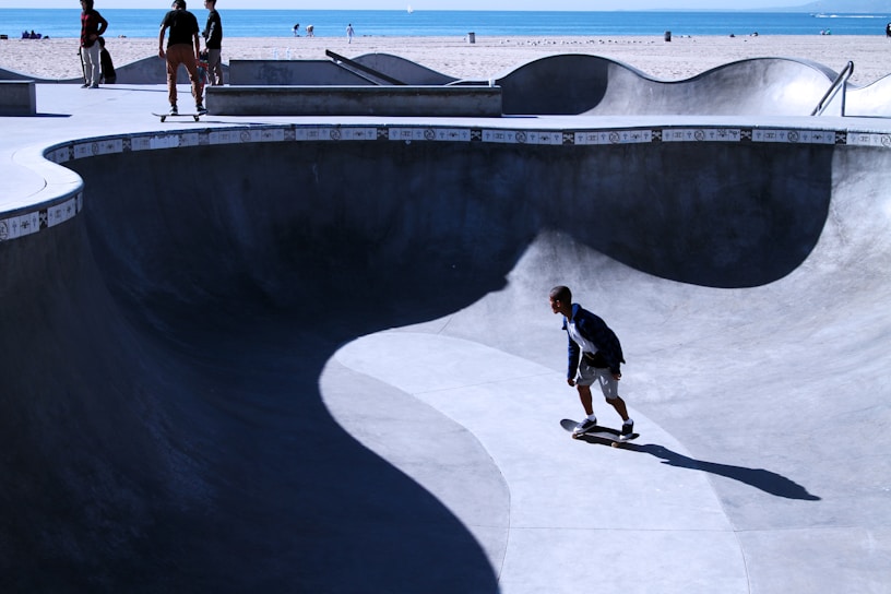 A smooth concrete skate bowl with skaters enjoying the flow under a bright blue sky.
