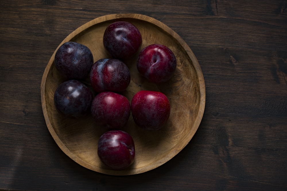 red plum fruits on round brown wooden plate